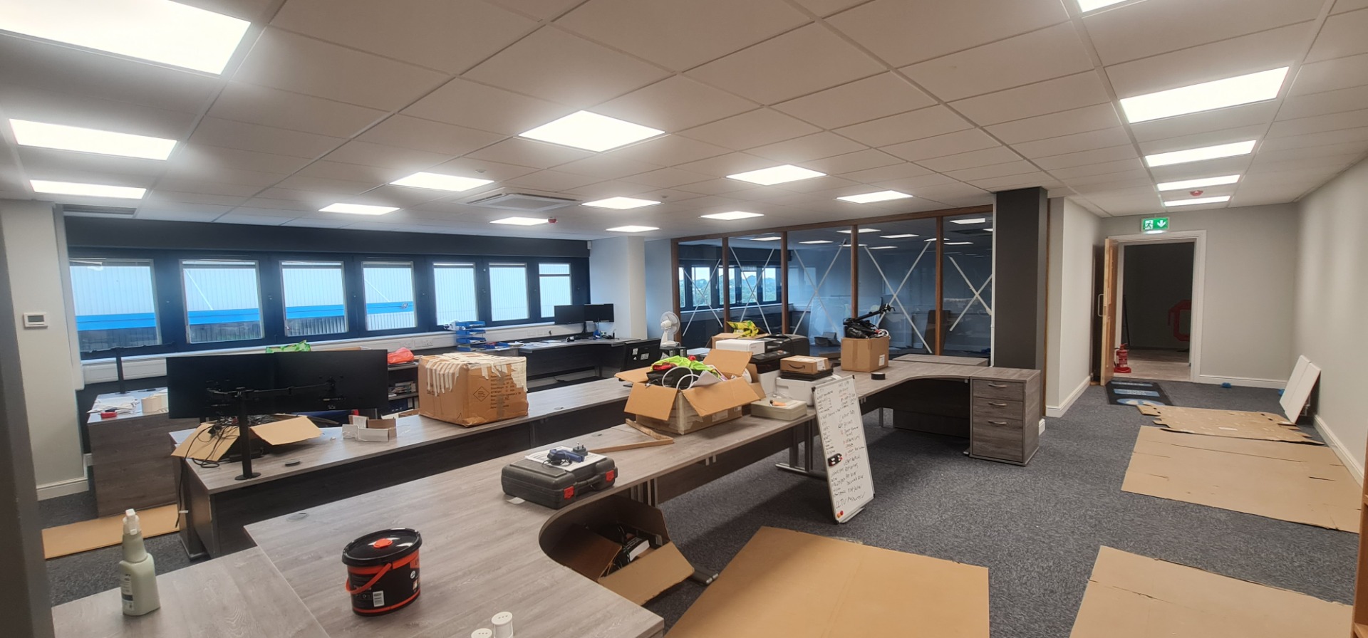 Office workspace with desks, monitors, scattered boxes, and construction materials during renovation.