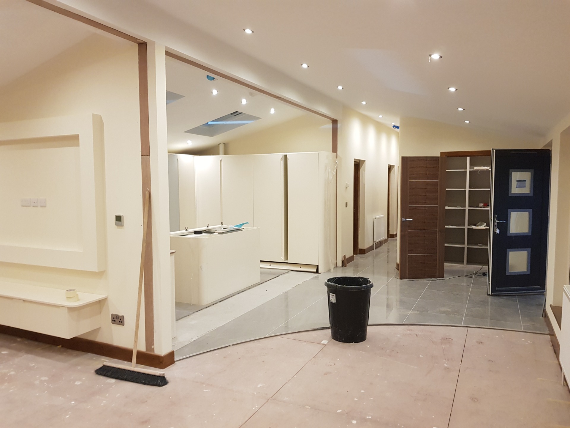 Bright unfinished interior with recessed lights, white cabinetry, tiled floor, and a dark door and shelving.