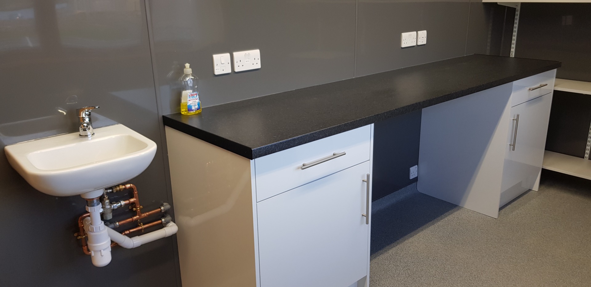 Modern bathroom vanity with dark countertop, white sink, chrome tap, and wall sockets above.